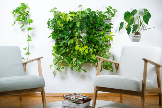 Wohnzimmer mit zwei hellgrauen Sesseln und einer großen grünen Pflanzenwand aus vertical pot Wandtöpfen – Urban Jungle Look im modernen Interior